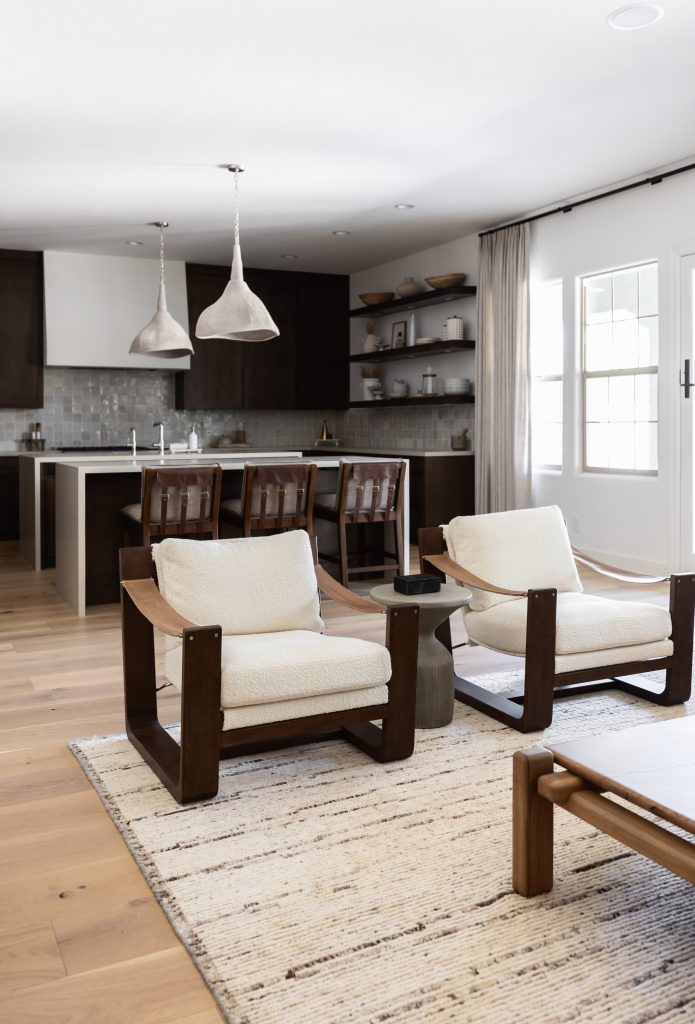 Open-plan living room and kitchen with neutral colors, wood furniture, two armchairs, and pendant lights over a kitchen island. — Living with Lolo.