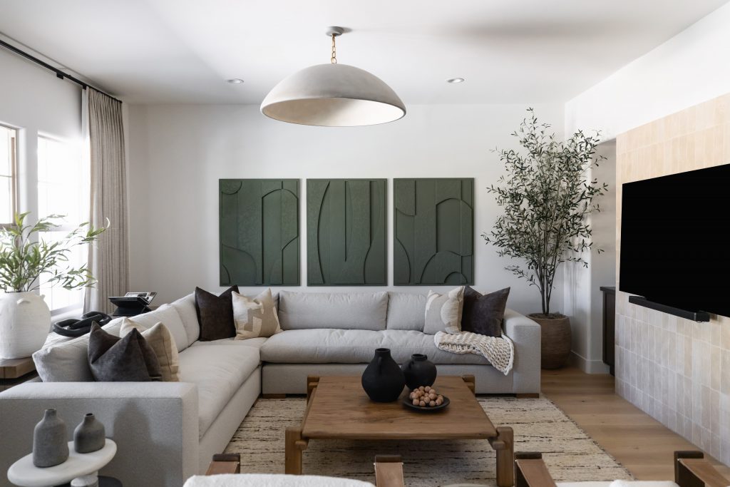 Modern living room with a large sectional sofa, wooden coffee table, wall art, potted plant, neutral decor, and flat screen TV—Living with Lolo.