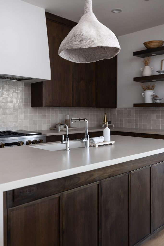Modern kitchen with dark wood cabinets, white island countertop, chrome faucet, large textured pendant light, and open shelves—Living with Lolo.