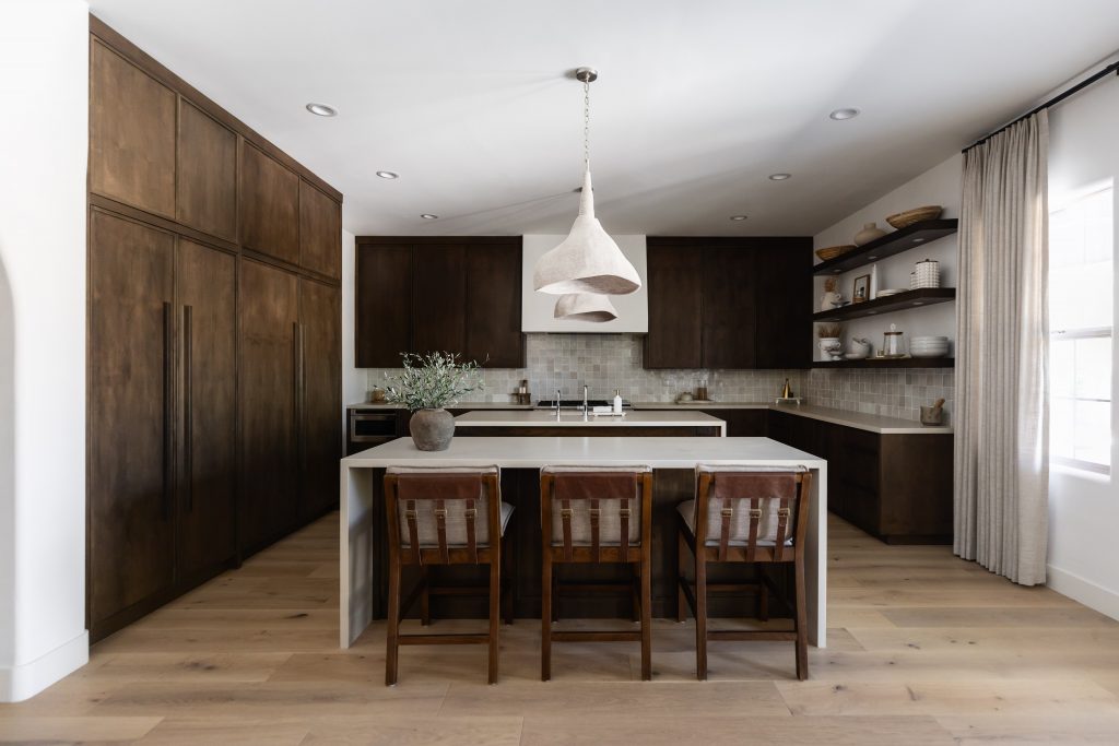 Modern kitchen with dark wood cabinets, light countertops, open shelves, pendant light, and three wooden bar stools—Living with Lolo.