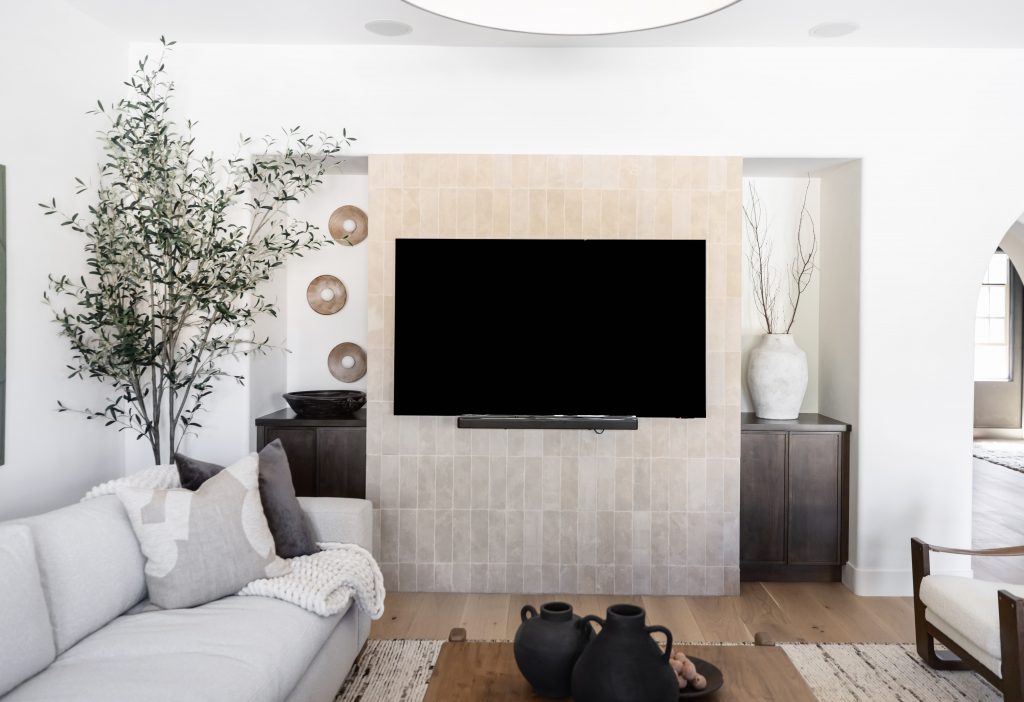 A living room with a wall-mounted TV, white sofa, neutral decor, wood coffee table, potted plant, and decorative vases.— Living with Lolo.