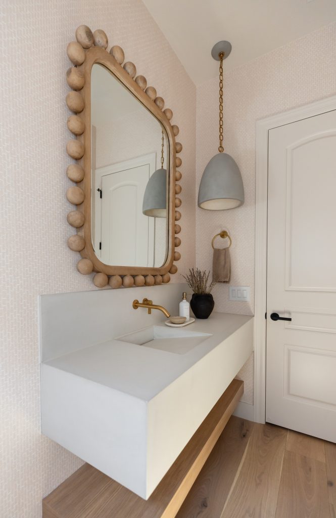 A modern bathroom vanity with a white rectangular sink, gold faucet, rounded mirror with wooden bead frame, and pendant light. — Living with Lolo.