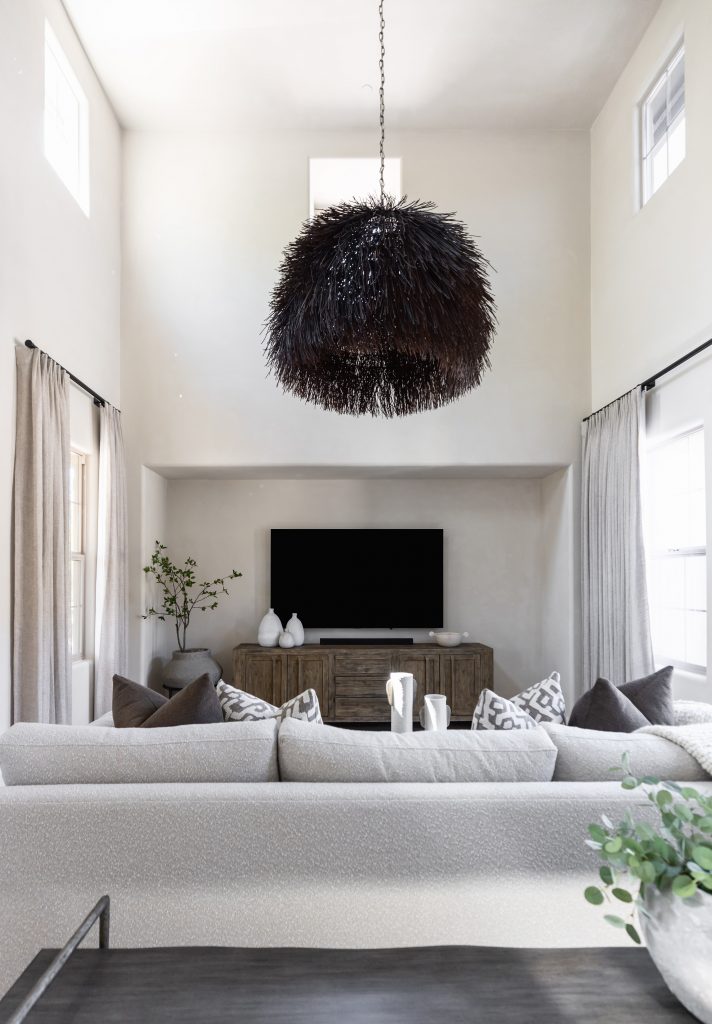 A modern living room with light walls, a black chandelier, beige sofa, wooden console with TV, and tall windows. — Living with Lolo.