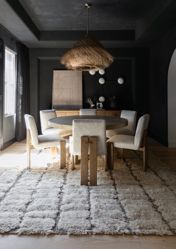 A dining room with six upholstered chairs around a wooden table, a textured rug, woven pendant light, and simple wall art— Living with Lolo.