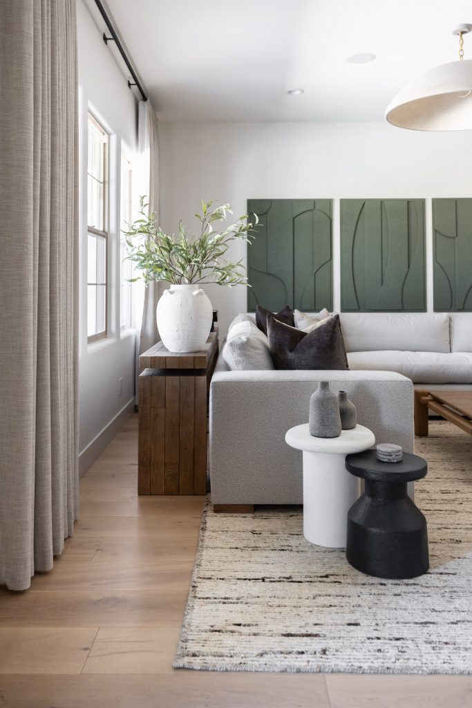 Modern living room with a light gray sectional sofa, minimalist side tables, green abstract wall art, and natural lighting—Living with Lolo.