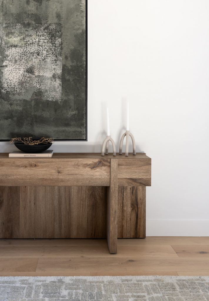 A wooden console table holds a shallow bowl of twigs and modern candleholders. A large abstract painting hangs on a white wall — Living with Lolo.