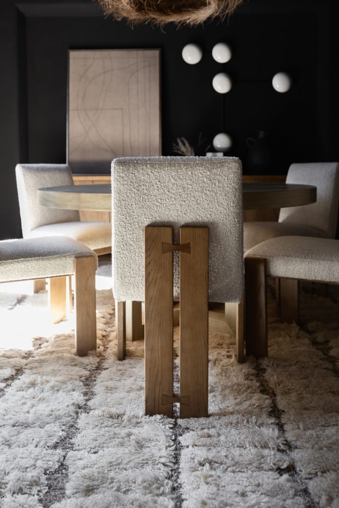 A dining room with cream upholstered chairs, a round wooden table, a textured rug, and abstract wall art in dark tones — Living with Lolo.