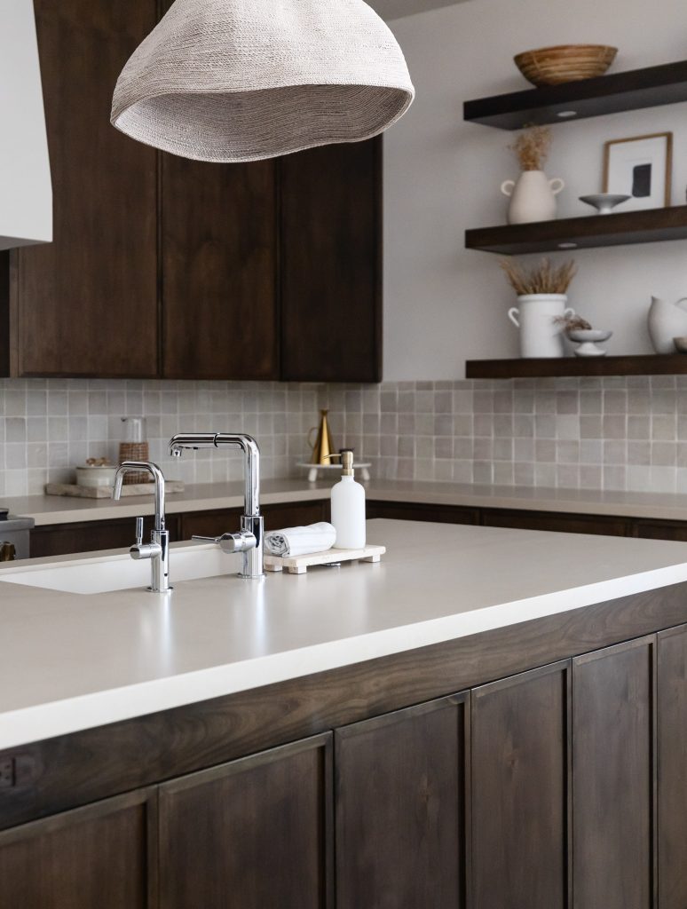 Modern kitchen with dark wood cabinets, white countertop, double sink with chrome faucet, open shelves, and a large pendant light—Living with Lolo.