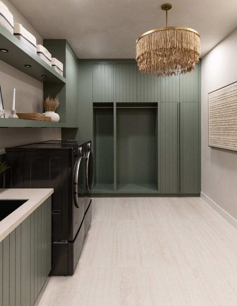 Laundry room with green cabinets, open shelves with baskets, black washer and dryer, light wood flooring, and neutral walls — Living with Lolo.