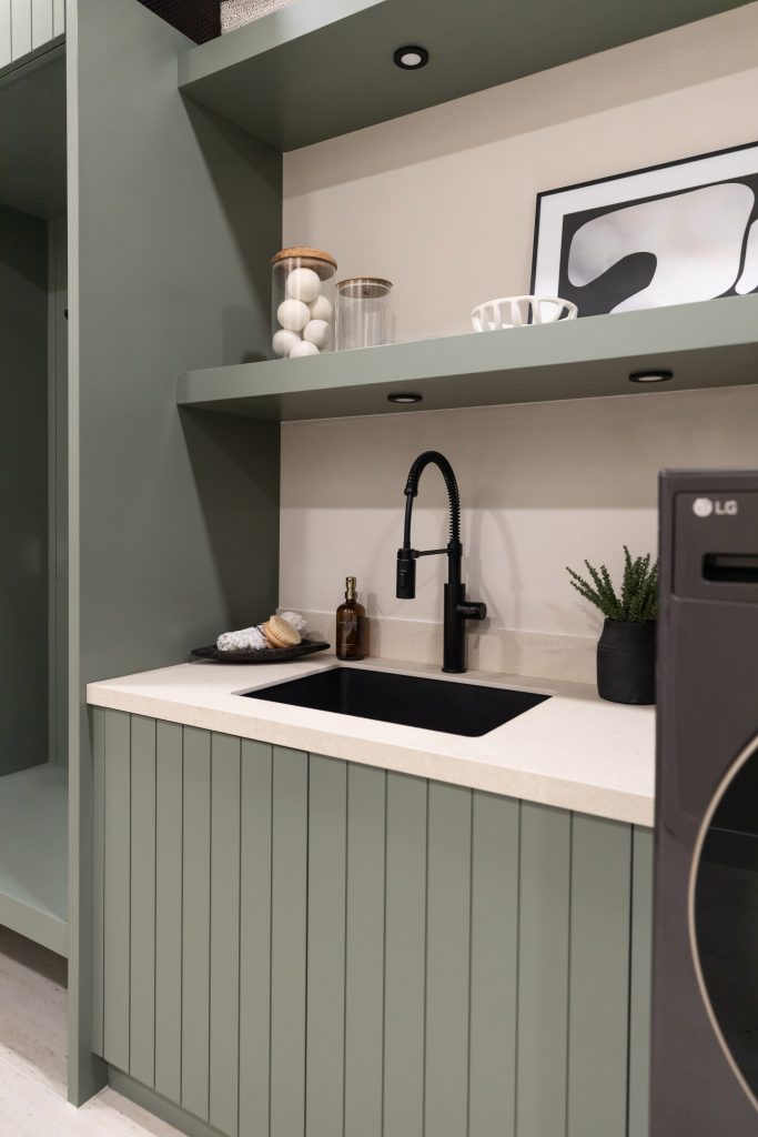 Sage green cabinets, a black faucet, a potted plant, and shelves with jars and framed art above the kitchen sink. — Living with Lolo.