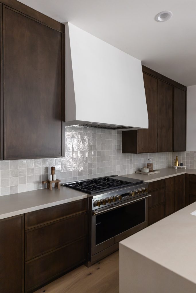 Modern kitchen with dark wood cabinets, white tile backsplash, stainless steel range, and a white vent hood—Living with Lolo.