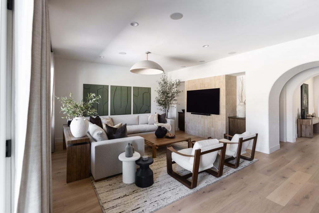 Modern living room with a sectional sofa, two armchairs, wooden coffee table, large TV, light wood floors, and wall art—Living with Lolo.
