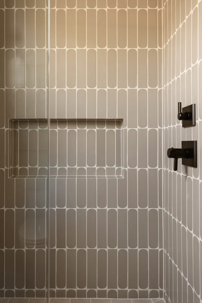 Shower wall with beige and white oval-patterned tiles, a built-in shelf niche, and black matte shower fixtures on the right—Living with Lolo.