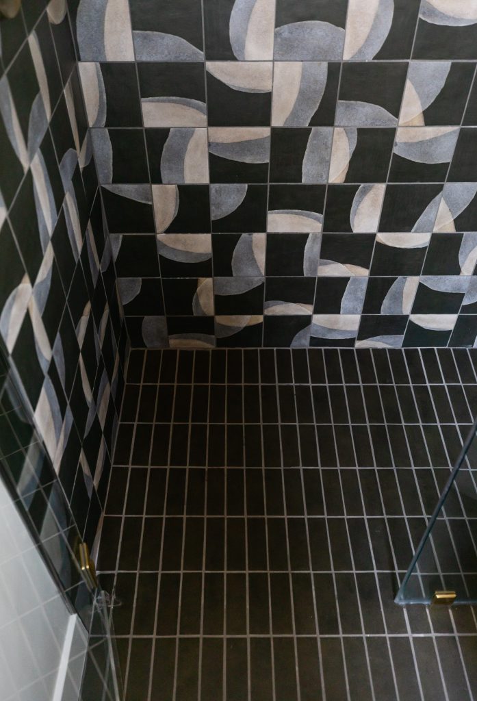 A shower area with dark floor tiles and black wall tiles featuring a geometric pattern of white and grey semicircles—Living with Lolo.