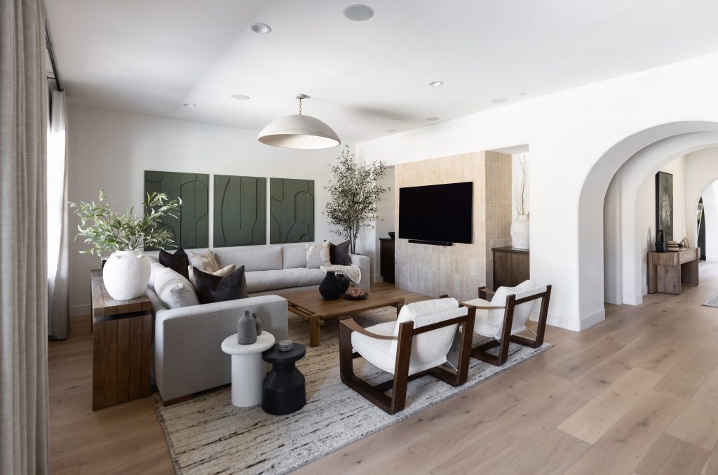 Modern living room with a large sectional sofa, two armchairs, wall-mounted TV, light wood flooring, and an arched doorway—Living with Lolo.