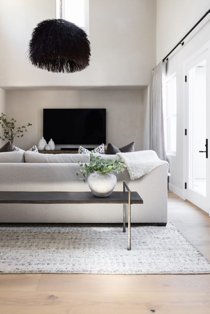 A light gray sofa faces a black wall-mounted TV, with a black pendant light overhead and a plant in a silver pot behind the sofa. — Living with Lolo.