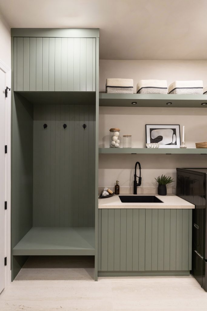 Modern laundry room with sage green cabinets, open shelves, a built-in bench with hooks, black faucet, and small sink — Living with Lolo.