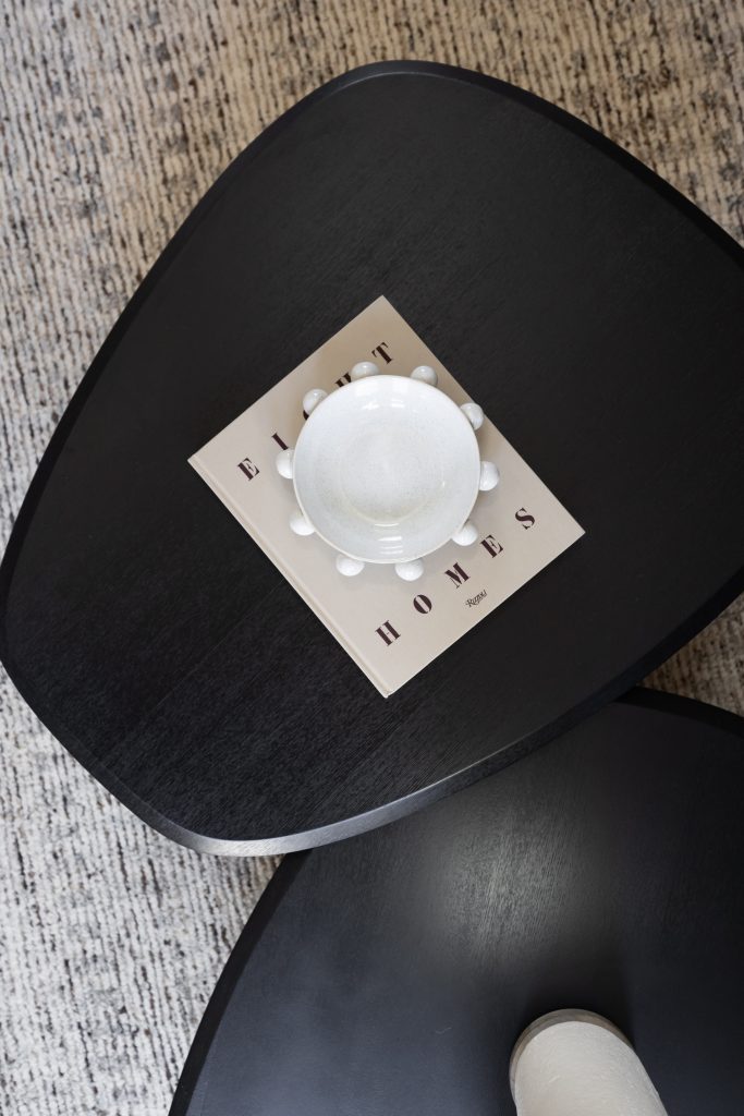 A white ceramic bowl rests on a book atop a black triangular coffee table next to another matching table over a textured carpet. — Living with Lolo.