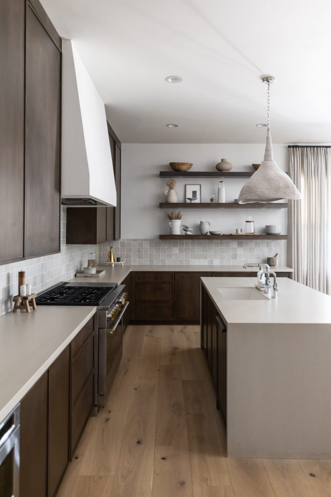 Modern kitchen with dark wood cabinets, light countertops, open shelves with decor, a large pendant light, and light wood flooring—Living with Lolo.