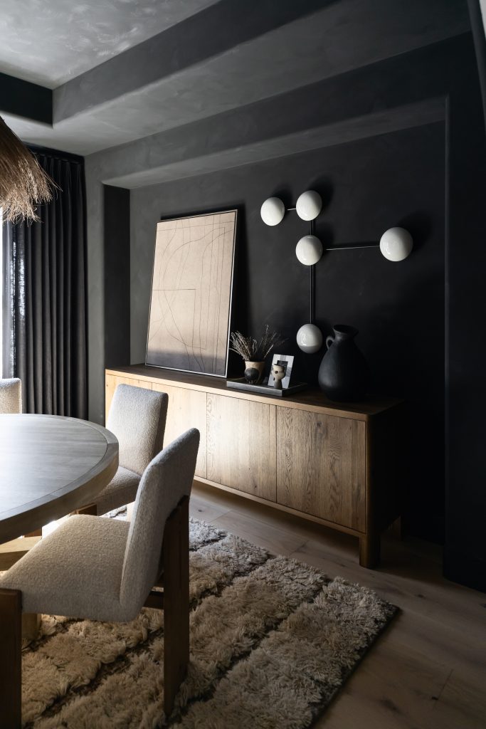 A modern dining room with a round table, textured chairs, shaggy rug, wooden sideboard, and abstract wall art in neutral tones. — Living with Lolo.