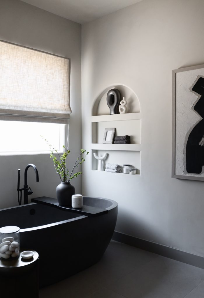 Modern bathroom with a black freestanding tub, black fixtures, niche shelves, a vase with greenery, and monochrome artwork. — Living with Lolo.