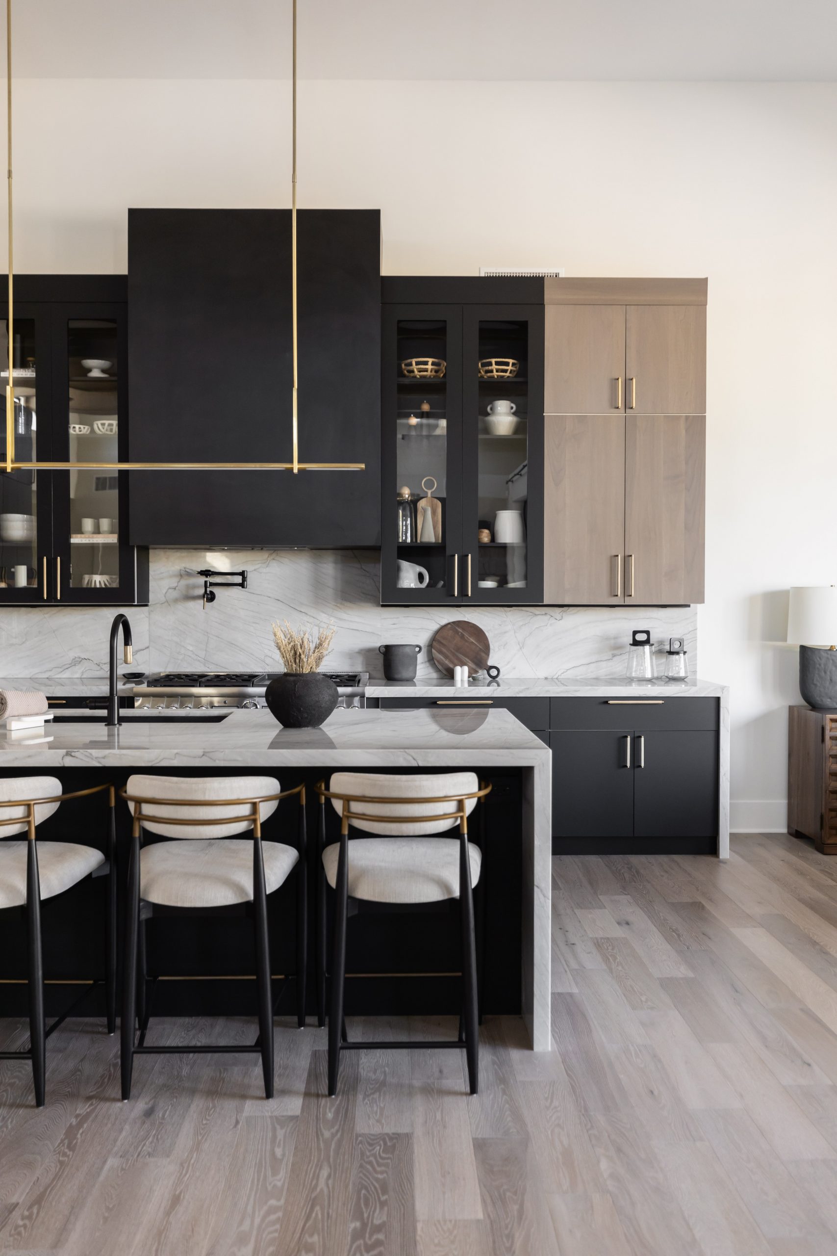 Modern kitchen with black and wood cabinets, marble backsplash, black island with three bar stools, and minimal decor.— Living with Lolo.