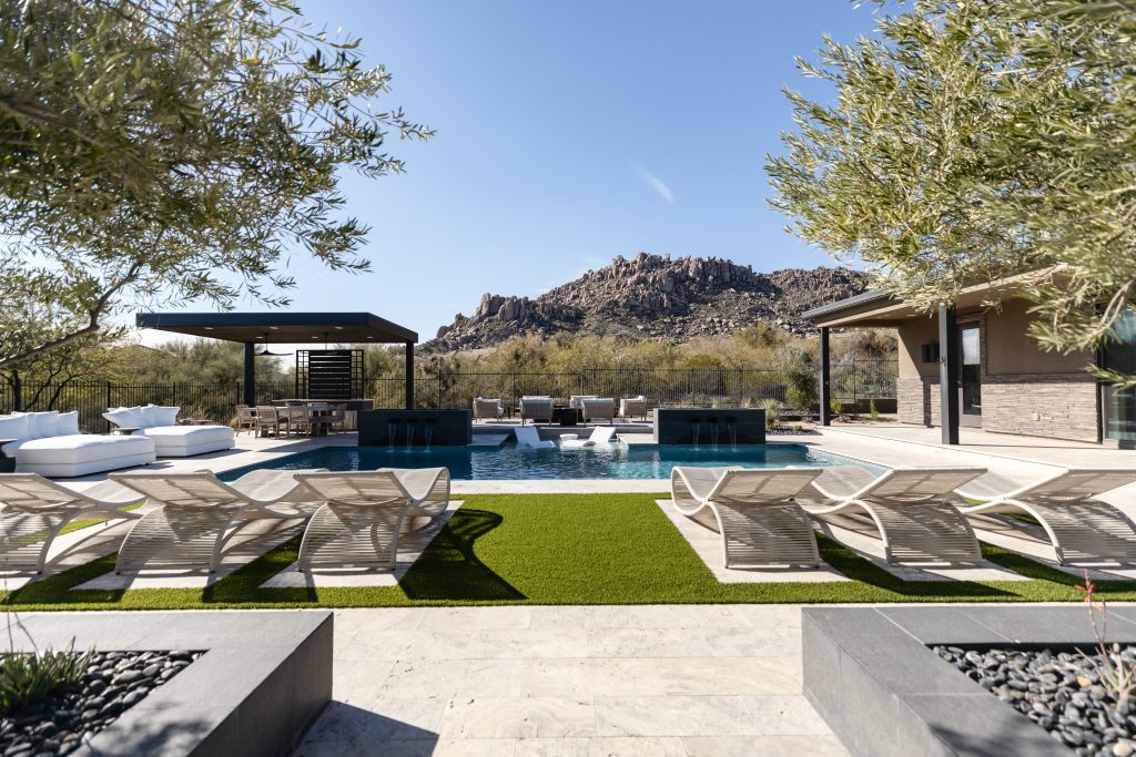 Modern outdoor pool area with lounge chairs and shaded seating; mountains are visible in the background. — Living with Lolo.
