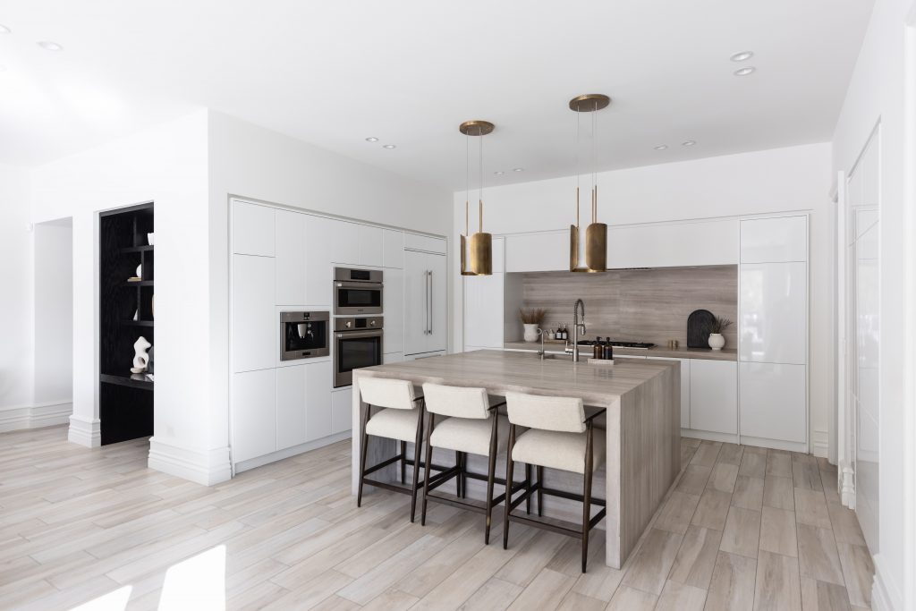 Modern kitchen featuring white cabinets, a central island with four upholstered stools, pendant lights, and light wood flooring—Living with Lolo.