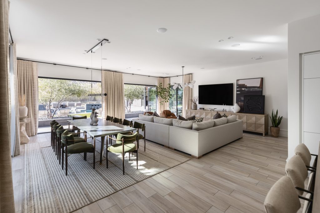 Open-plan living and dining area with large windows, a sectional sofa, green dining chairs, and light wood flooring — Living with Lolo.