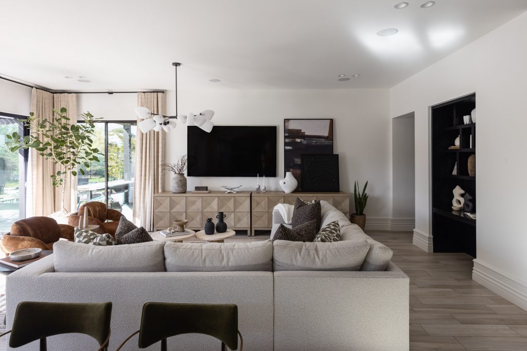 Modern living room featuring a large sectional sofa, wooden TV console, abstract decor, and floor-to-ceiling windows— Living with Lolo.