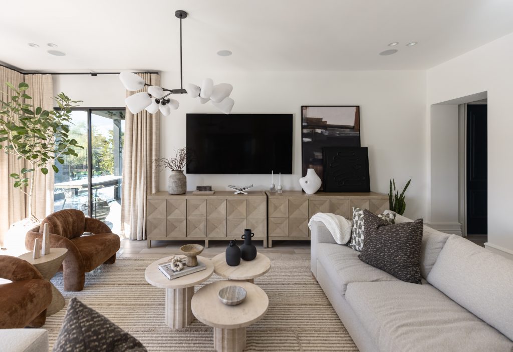 Modern living room with a wall-mounted TV, light gray sofa, brown chairs, round coffee tables, and minimalist decor accents—Living with Lolo.