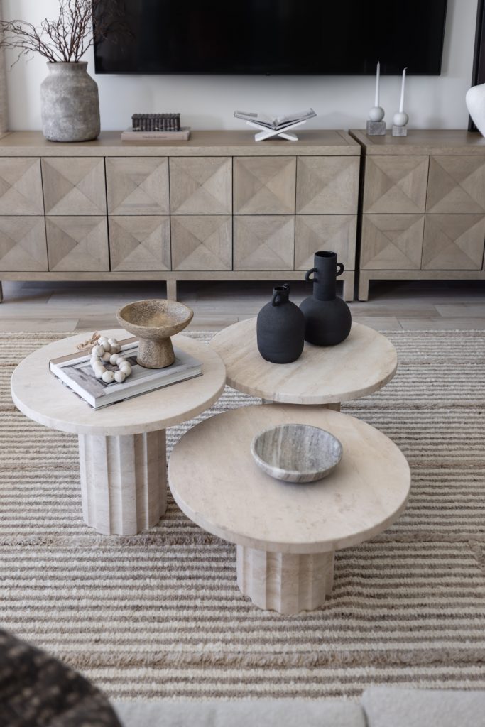 Three round stone coffee tables with decorative objects rest on a striped rug in front of a wood console—Living with Lolo.