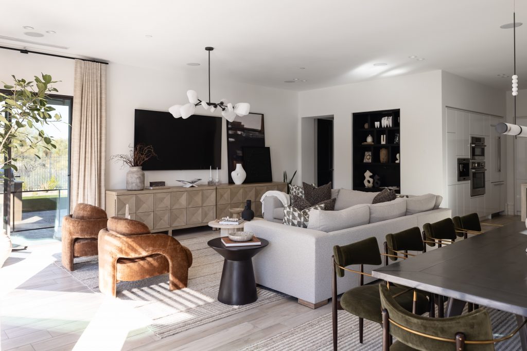 Open-concept living room with neutral colors, large sectional sofa, brown armchairs, wall-mounted TV, and glass doors.— Living with Lolo.