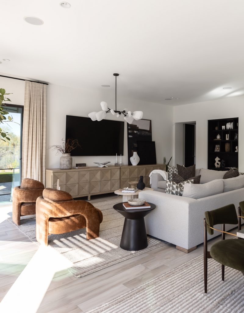 A living room with a large TV, beige sectional sofa, two brown chairs, a black side table, and neutral decor. — Living with Lolo.