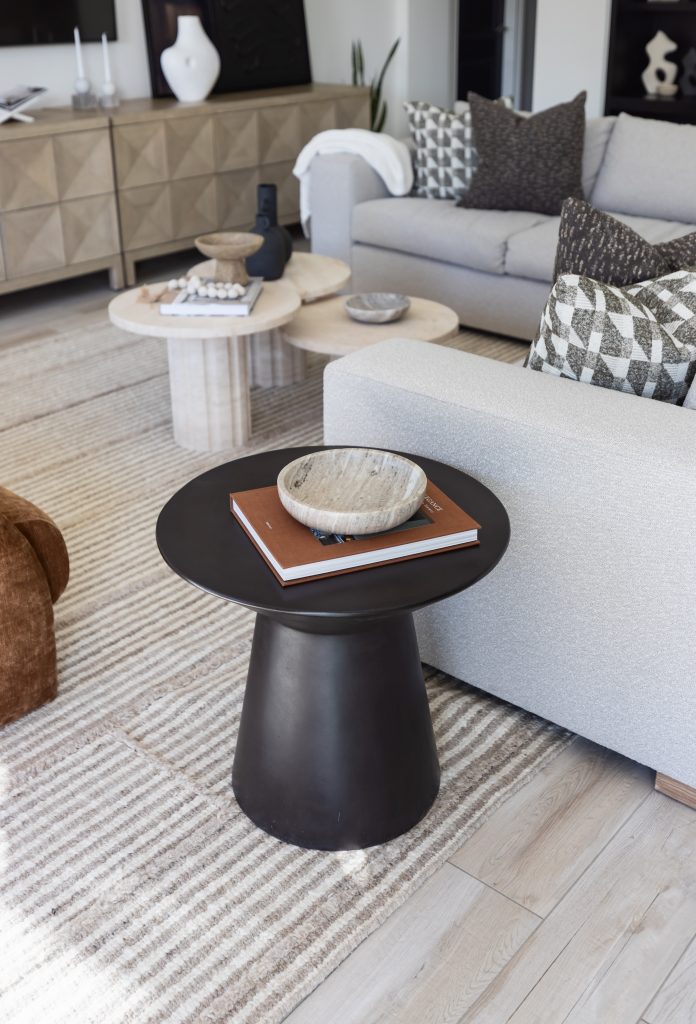 Neutral-toned sofas, patterned pillows, a black side table with a bowl and book, and nested coffee tables sit on a striped rug. — Living with Lolo.