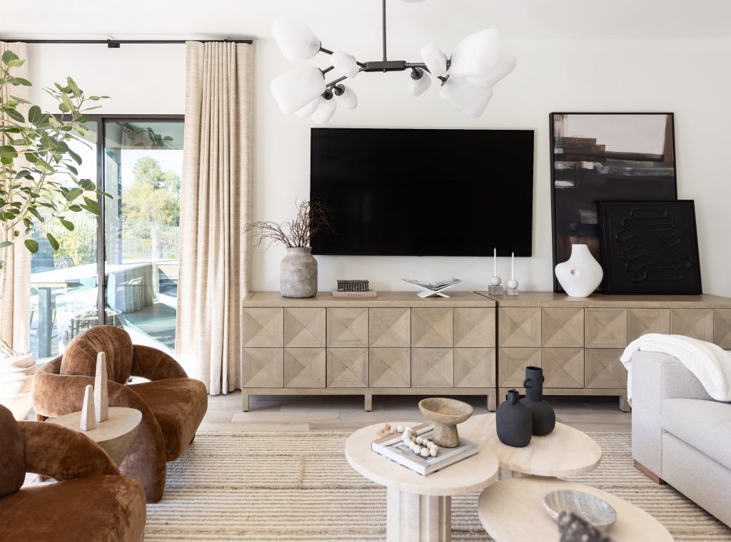 Modern living room featuring a wall-mounted TV, geometric sideboard, abstract art, round tables, and a modern light fixture—Living with Lolo.