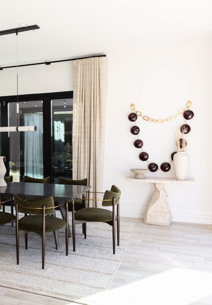 A dining room with a dark wood table, green chairs, a light rug, a console table with vases, and wall art of round shapes— Living with Lolo.