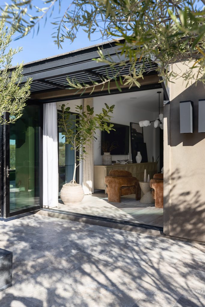 A modern living room features large glass doors to a stone patio, with brown chairs and a potted tree inside. — Living with Lolo.