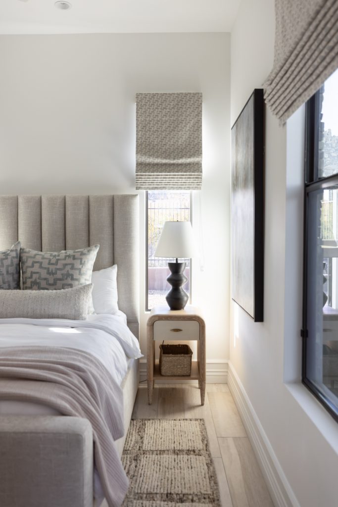 A neatly made bed with neutral bedding is next to a nightstand holding a black lamp and a small basket. — Living with Lolo.