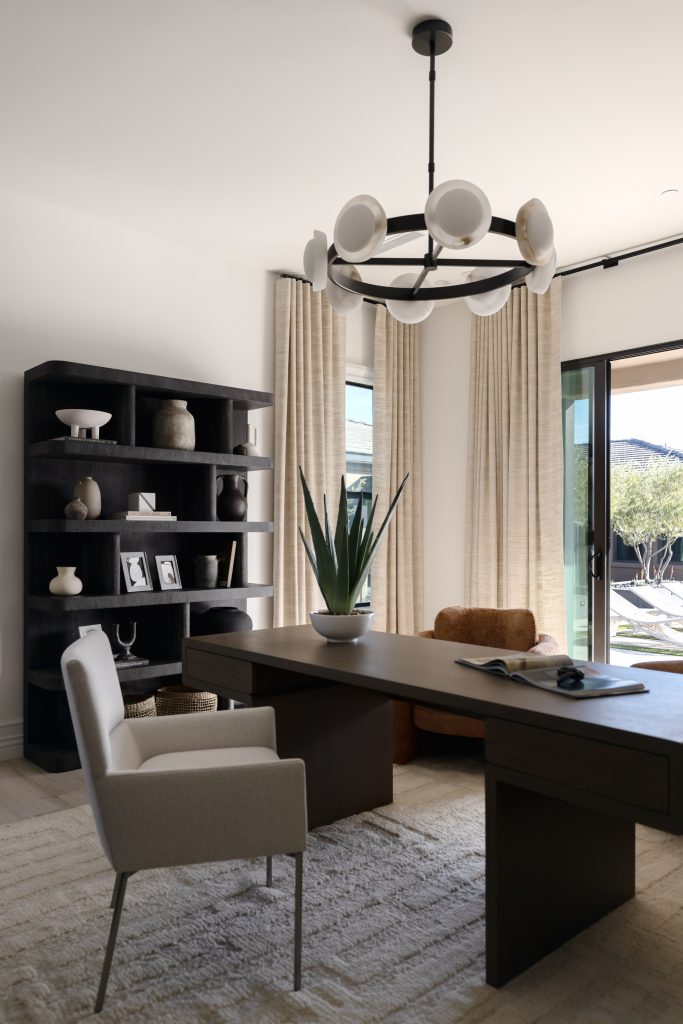 Dark desk, white chair, brown armchair, potted plant, black shelves, large windows with beige curtains, circular light fixture—Living with Lolo.