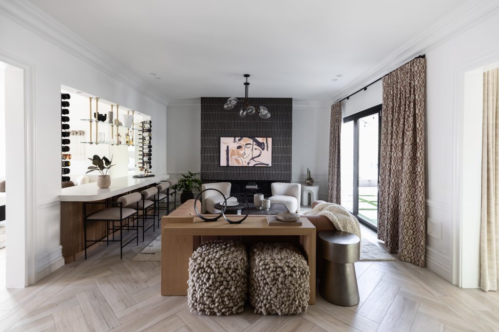 Living room with neutral decor, a sofa facing a black-tiled fireplace, abstract art, bar stools at a kitchen counter, and patterned curtains—Living with Lolo.