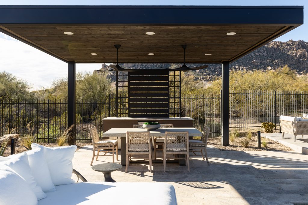 Outdoor patio with a wooden table, chairs, and a modern canopy, set in a desert landscape with mountains in the distance—Living with Lolo.