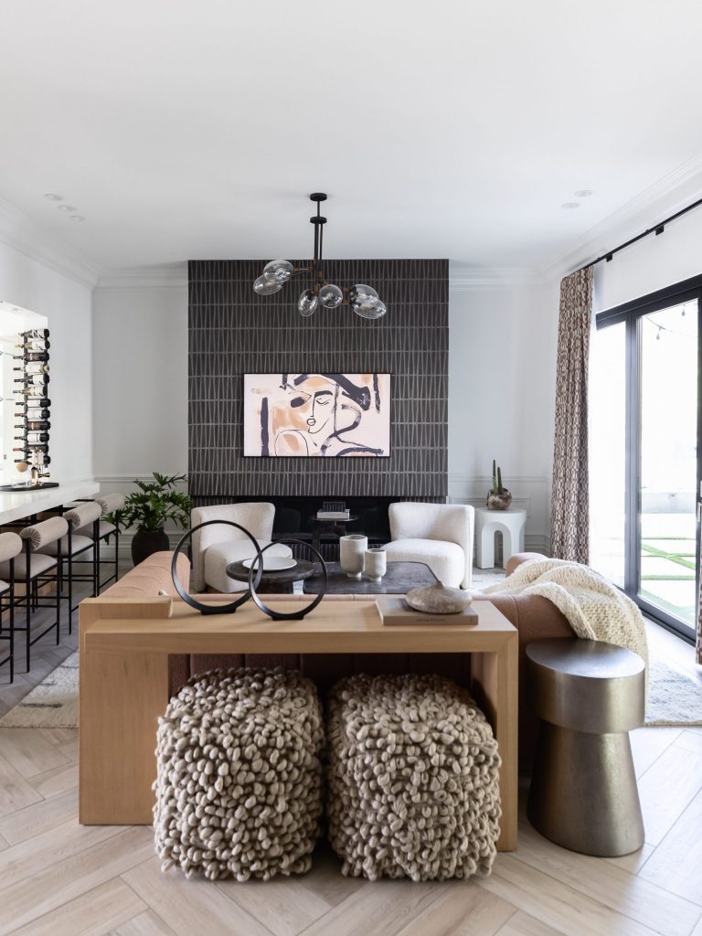 Modern living room featuring neutral tones, abstract wall art, textured poufs, a wood console, black tiled fireplace, and large windows—Living with Lolo.