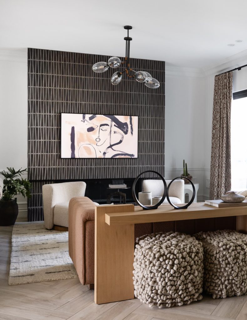 Modern living room with abstract art on a patterned wall, neutral furniture, textured ottomans, wooden console, and curtained window—Living with Lolo.
