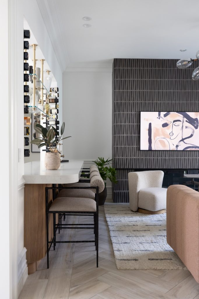 Modern living space with neutral tones, a bar area and stools, abstract wall art, a textured accent wall, and contemporary furniture — Living with Lolo.