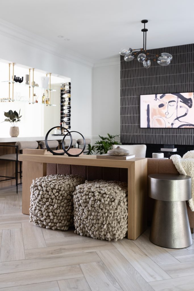 A wooden console table sits with two textured ottomans, a metallic side table, abstract wall art, and modern lighting—Living with Lolo.