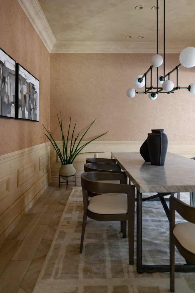A modern dining room with a marble table, wooden chairs, abstract wall art, potted plant, and geometric chandelier. — Living with Lolo.