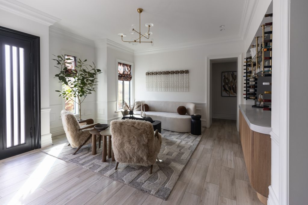 Modern living room featuring light wood floors, a beige sofa, two fur-covered chairs, a round coffee table, and wall-mounted wine storage—Living with Lolo.