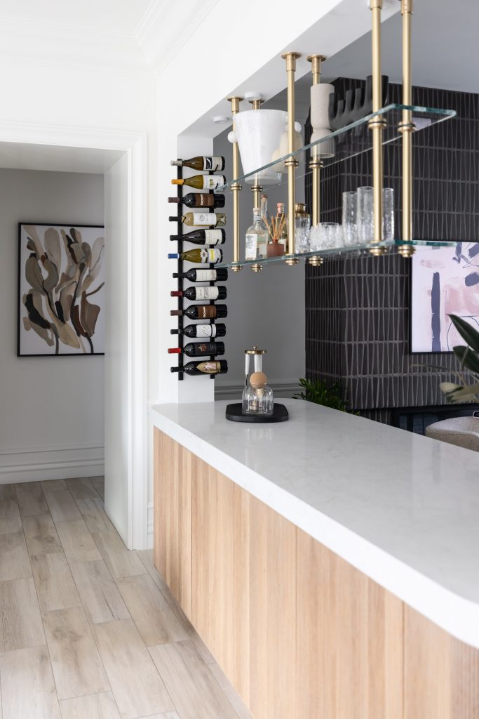 Modern home bar with a white marble countertop, wood paneling, hanging glasses, vertical wine rack, and geometric tile backsplash—Living with Lolo.
