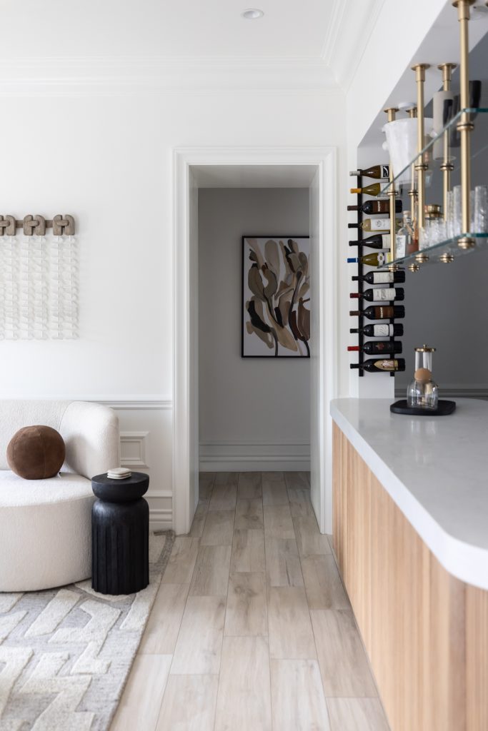 Light wood floors, a white curved sofa, black side table, marble countertop bar, and abstract wall art in the hallway. — Living with Lolo.